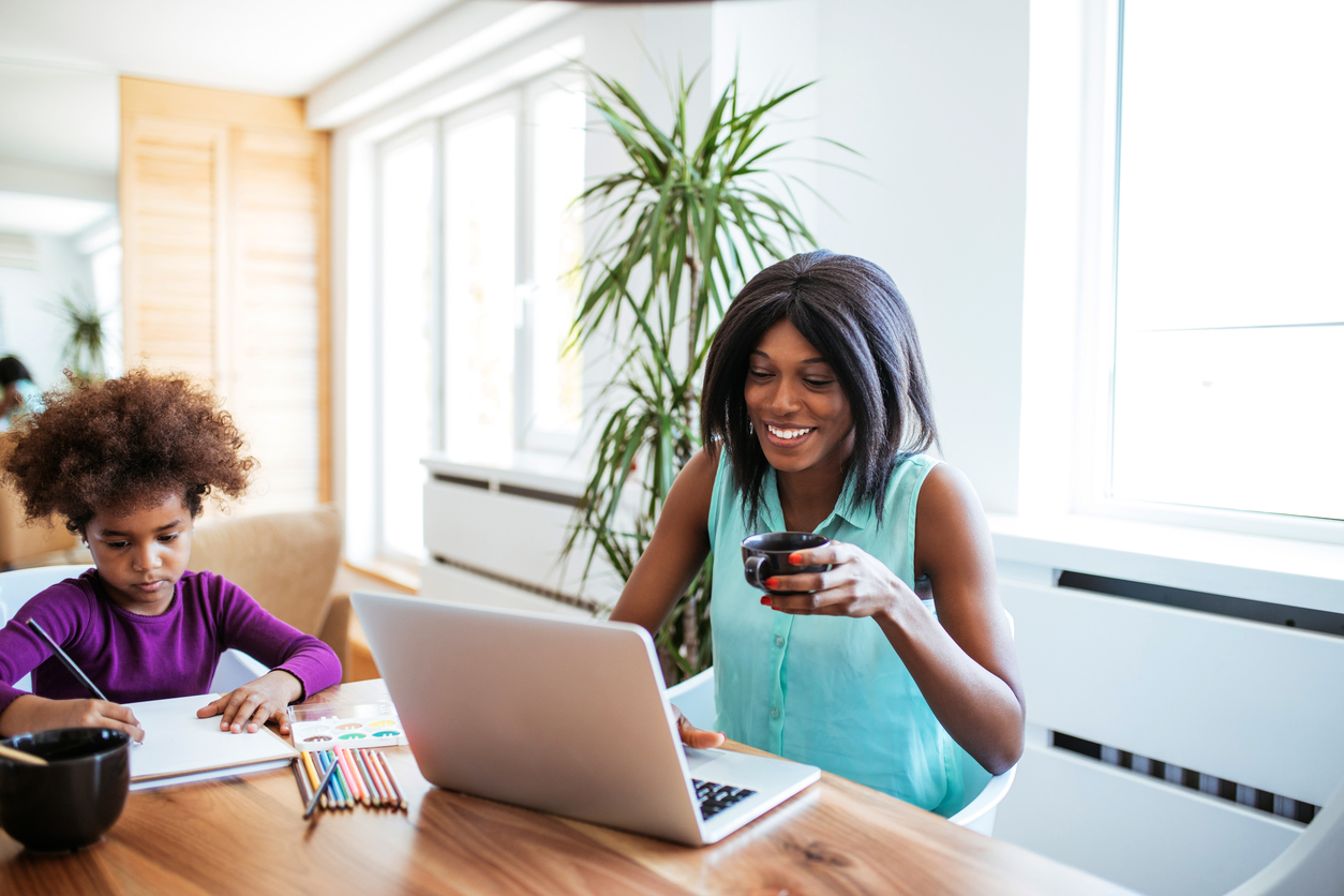 Young woman working on a laptop while her daughter is drawing.